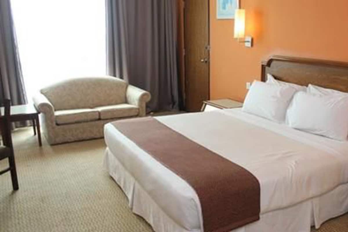 Habitación de hotel con una cama grande, una silla, una mesita de noche y una lámpara fijada a la pared.