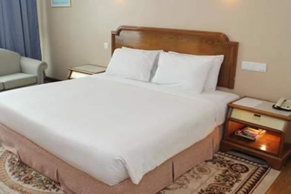 Una cama bien hecha con ropa blanca, un cabecero de madera y una mesita de noche con una lámpara y libros.