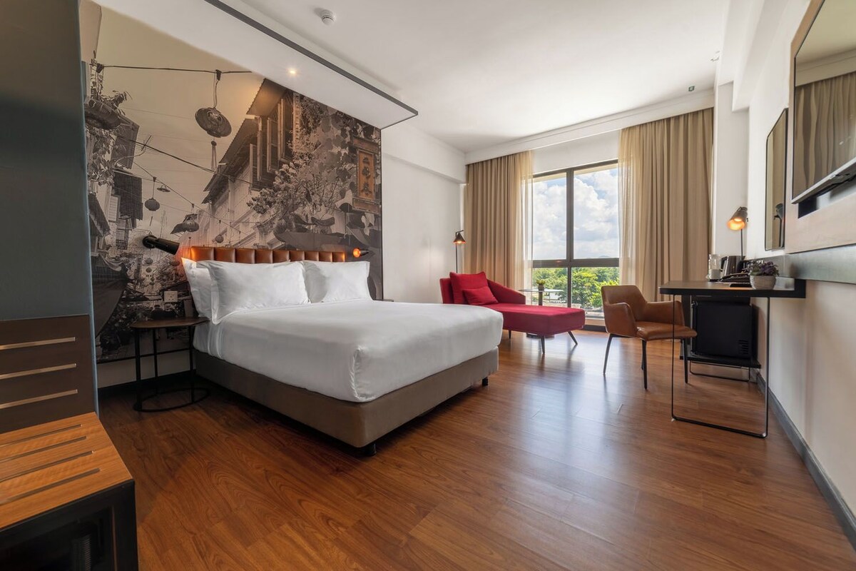 A modern hotel room with a large bed, a desk, a chair, and a TV.