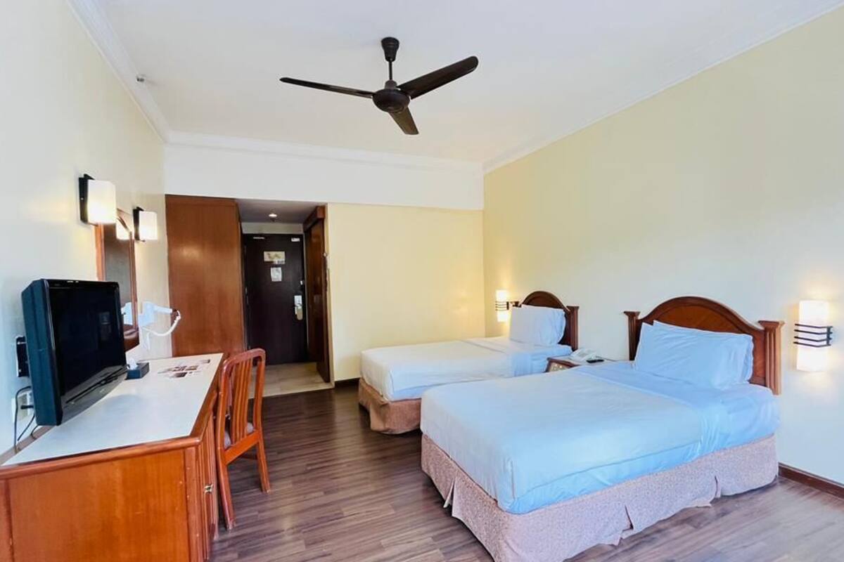 Habitación de hotel con escritorio, dos camas, ventilador de techo y puerta que da a otra habitación.