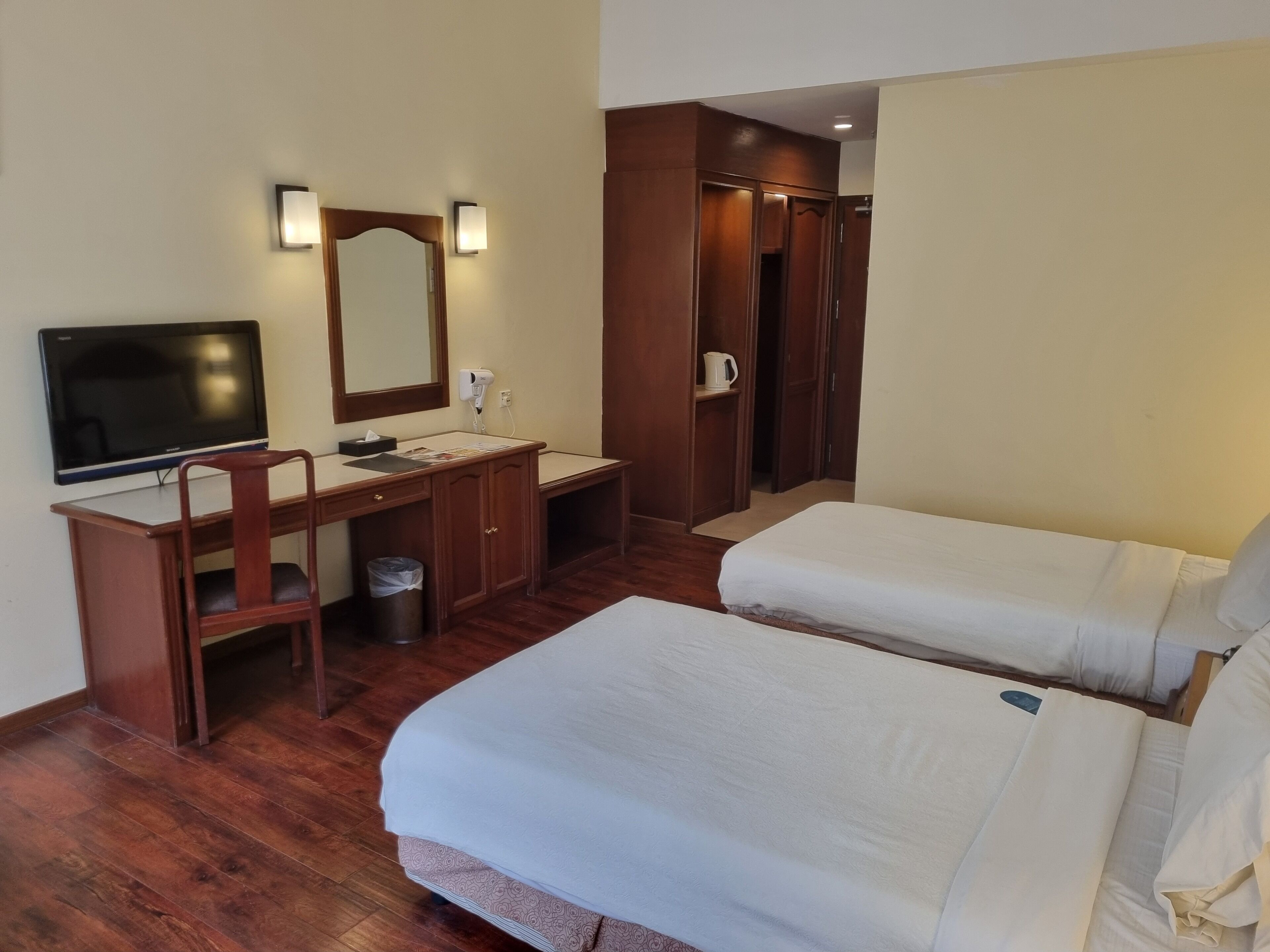 Habitación de hotel con dos camas, un escritorio con silla, televisión, espejo y armario.