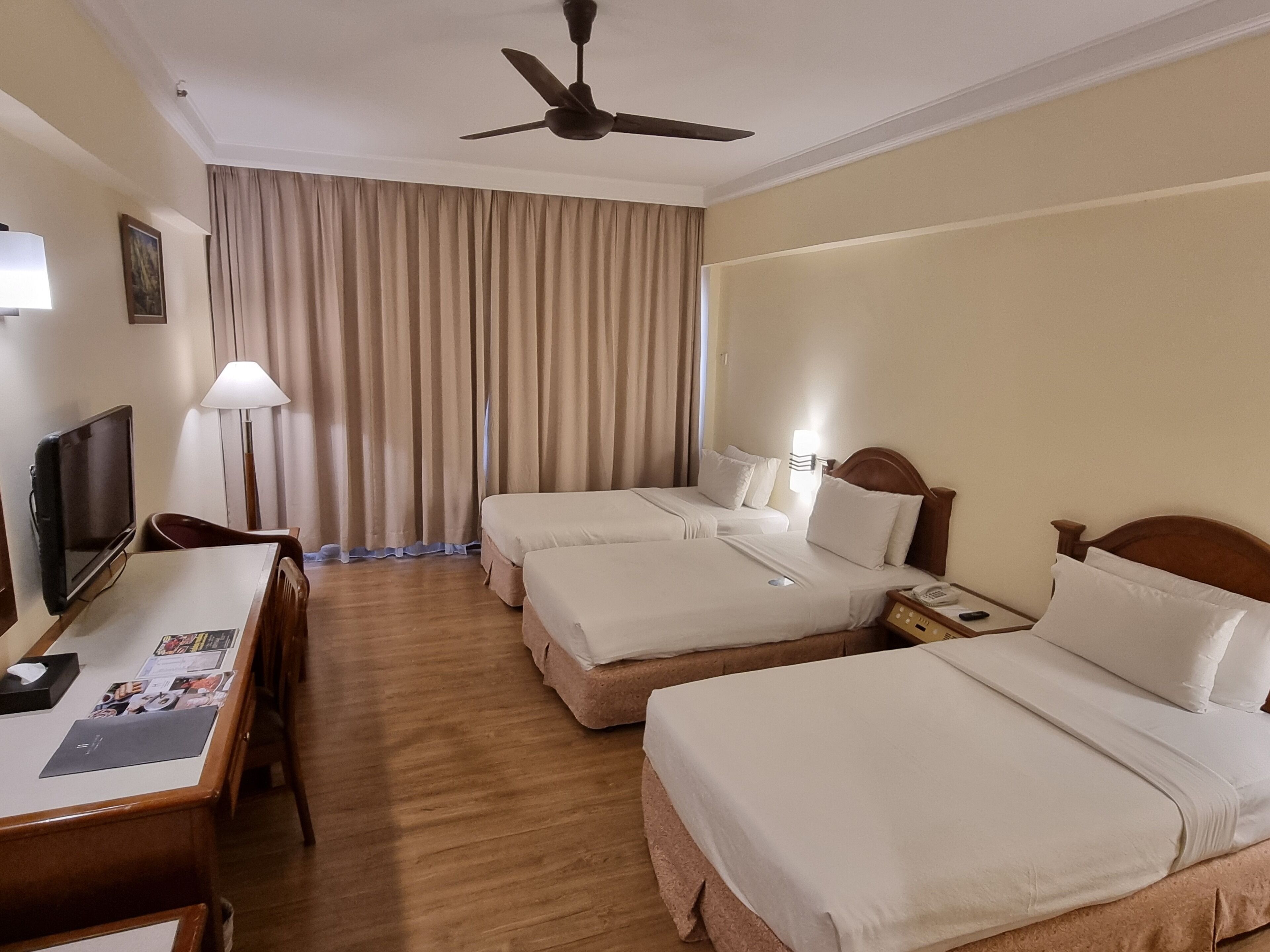 Une chambre d’hôtel avec deux lits, un bureau avec un ordinateur, une télévision et un ventilateur de plafond.