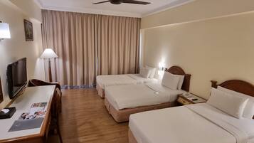 A hotel room with two beds, a desk with a computer, a TV, and a ceiling fan.