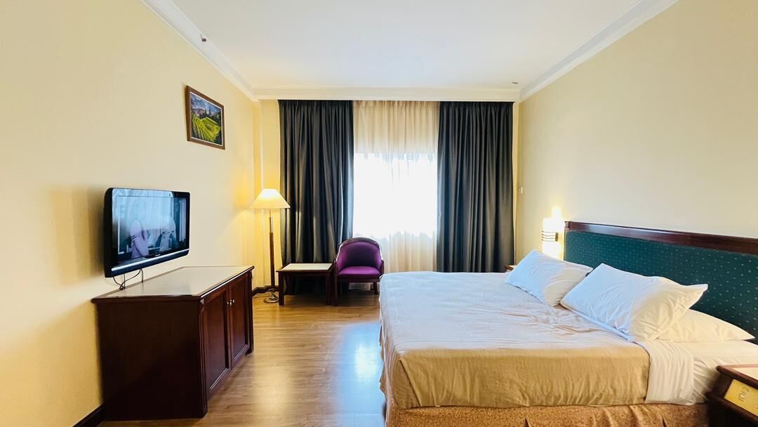 A hotel room with a bed, a TV, a desk, a chair, and curtains.