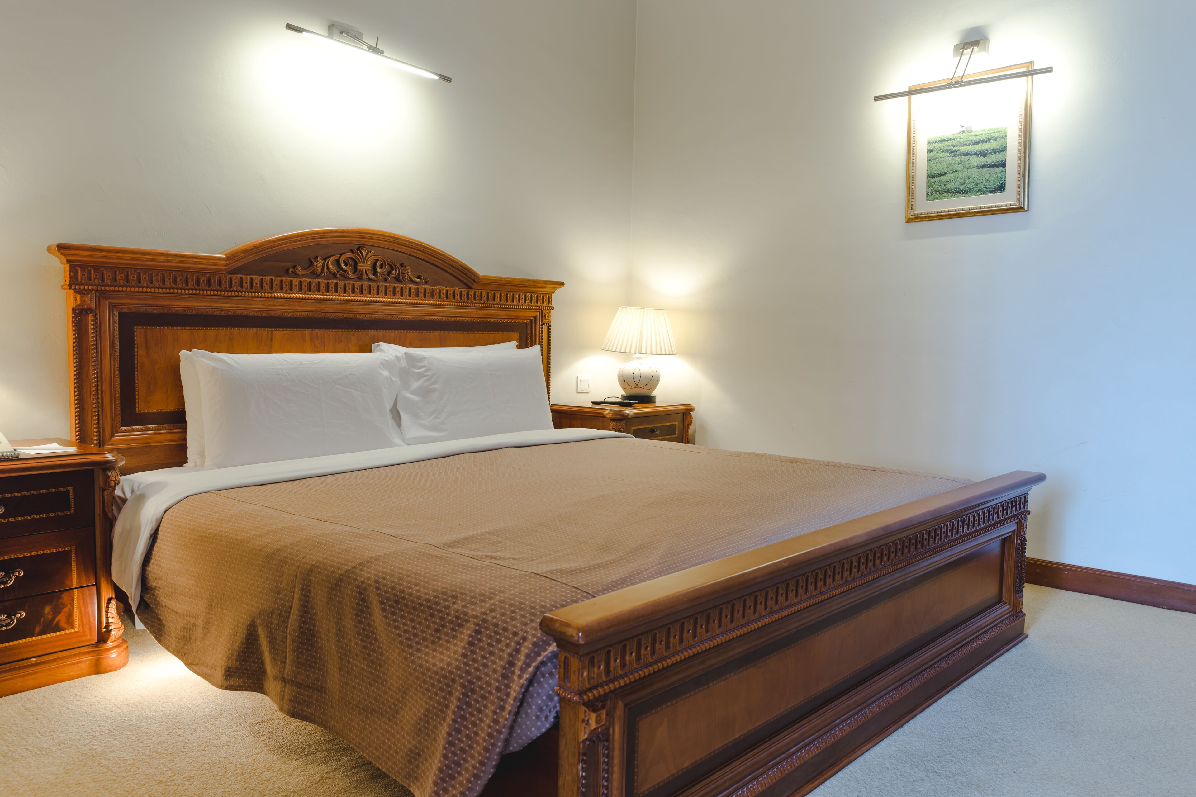 A neatly made bed with a wooden headboard, a bedside lamp, and a framed picture on the wall.