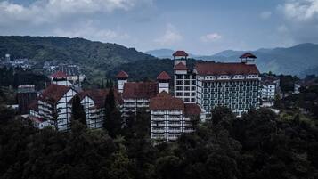 Um edifício grande, com vários andares, que combina estilos arquitetônicos tradicionais e modernos, rodeado por uma floresta densa.