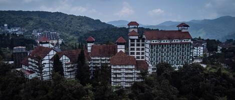 Un edificio grande de varios pisos con una mezcla de estilos arquitectónicos tradicionales y modernos, rodeado de un bosque denso.