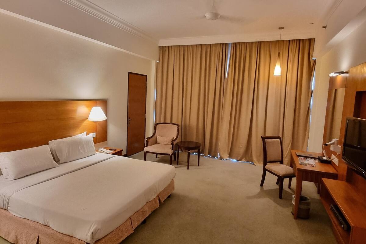 Una habitación de hotel con una cama grande, un escritorio, una silla, un televisor y un ventilador de techo.