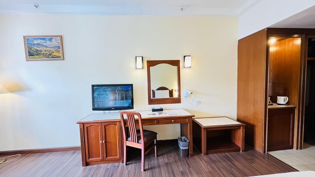 Une chambre d’hôtel avec un bureau en bois, une chaise, une télévision, un miroir et une armoire.