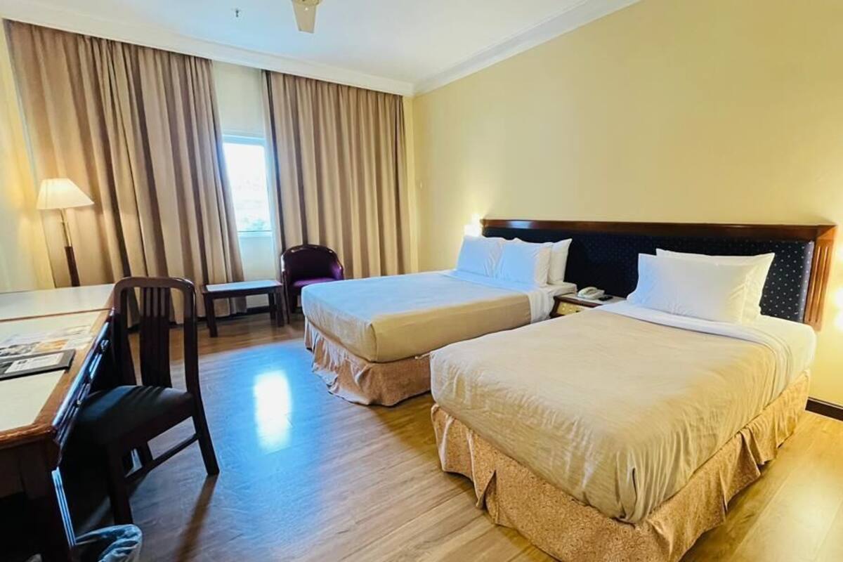 Una habitación de hotel con dos camas, un escritorio, una silla y una lámpara.