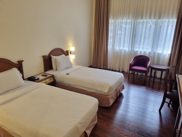 A hotel room with two beds, a desk, a chair, and a window with curtains.