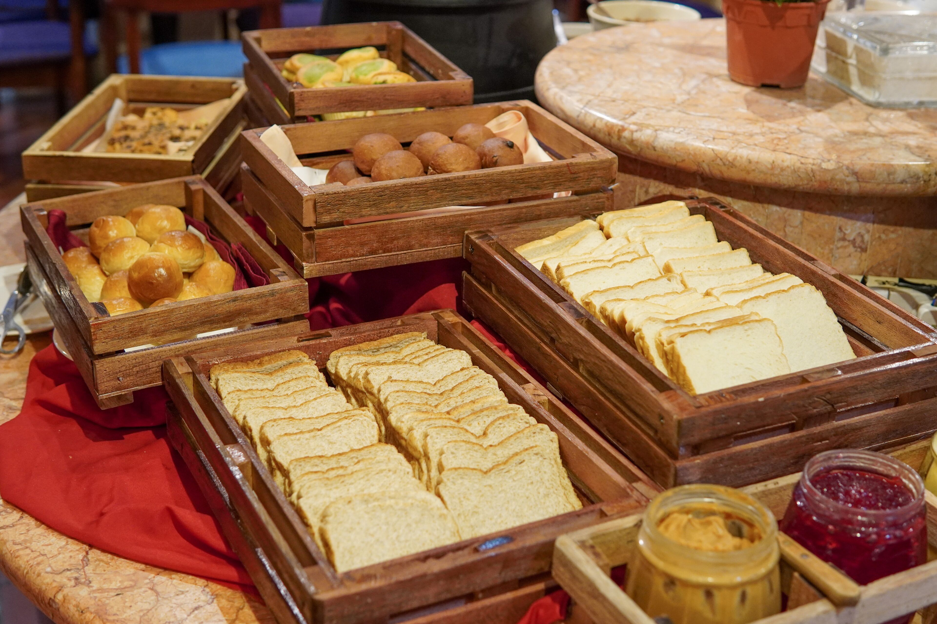 A buffet with various food items in wooden trays, including bread, pastries, and a jar of jam.