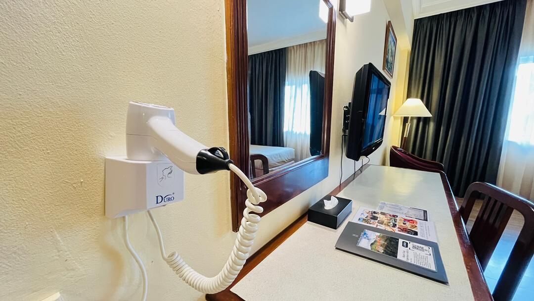A hotel room with a hairdryer, a television, a table with a menu, and a mirror reflecting the room.