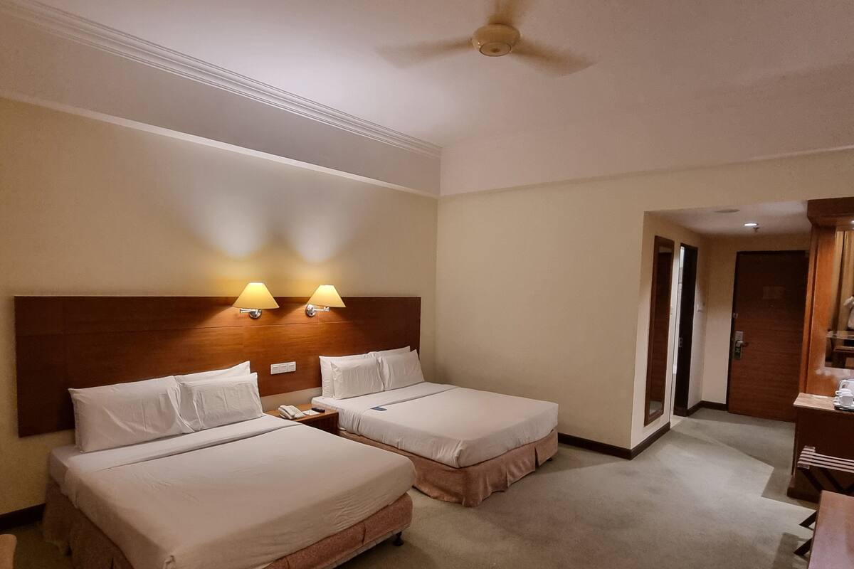 Habitación de hotel con dos camas, ventilador de techo y escritorio con silla.