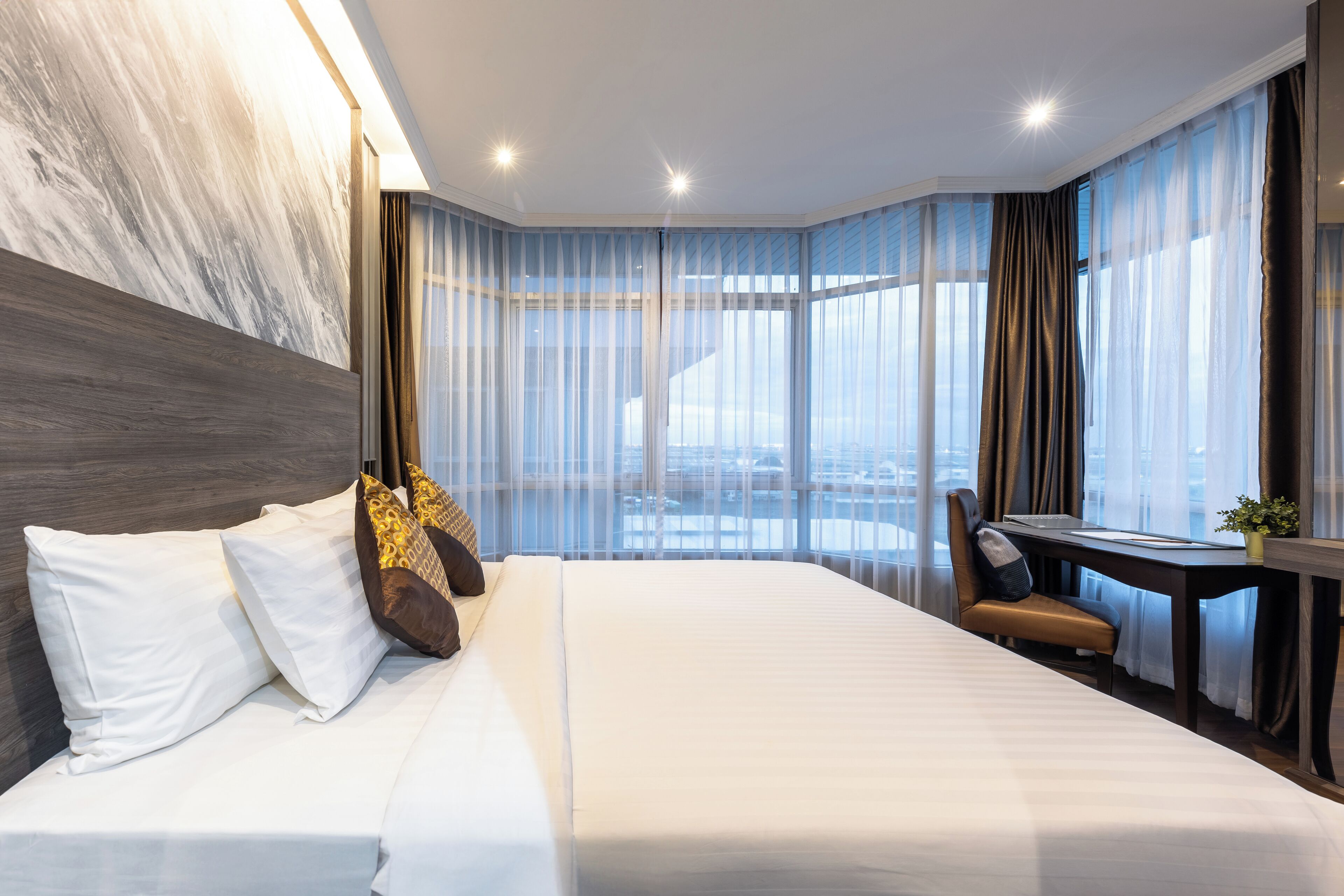 A modern hotel room with a large bed, a desk, and a view of the city.