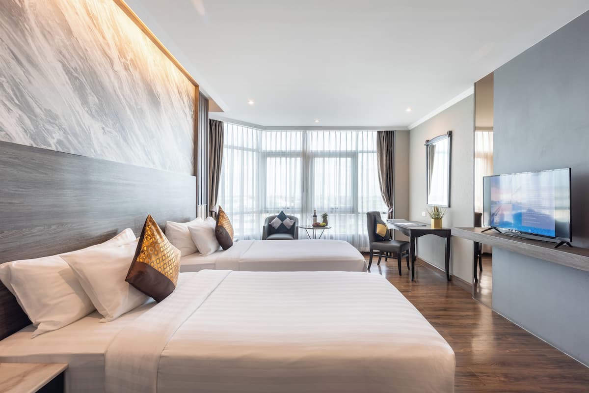 A hotel room with two beds, a desk, a TV, and a large window with curtains.