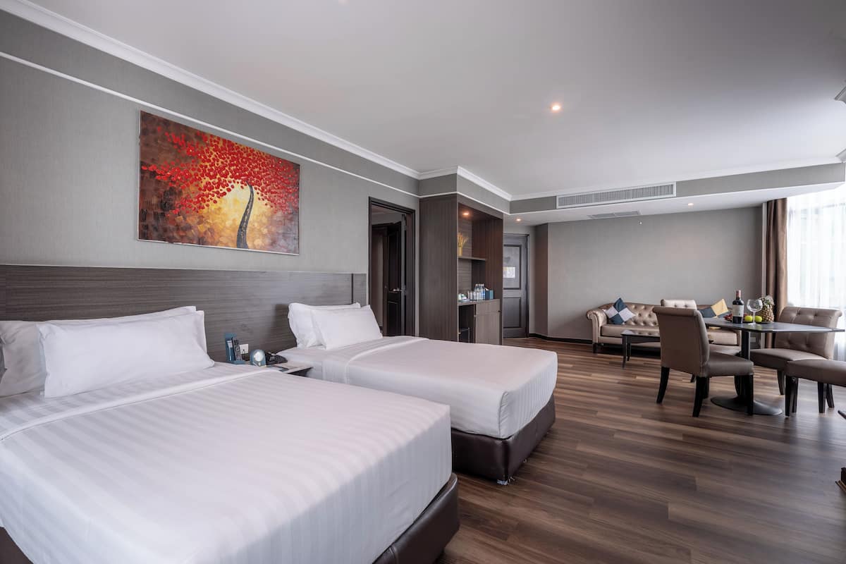 A hotel room with two beds, a dining area, and a painting on the wall.