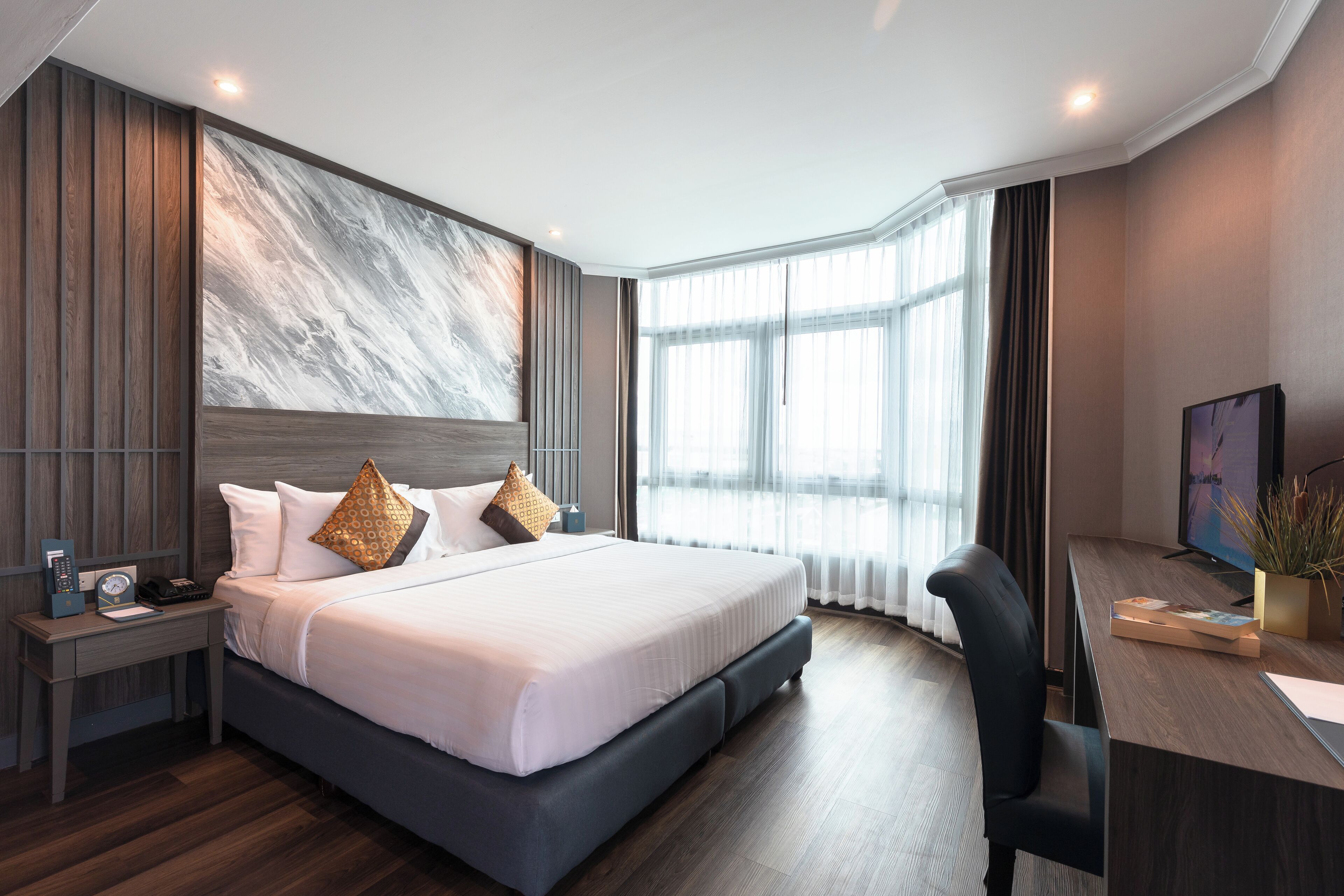 A modern hotel room with a large bed, a desk with a computer, and a large window with curtains.