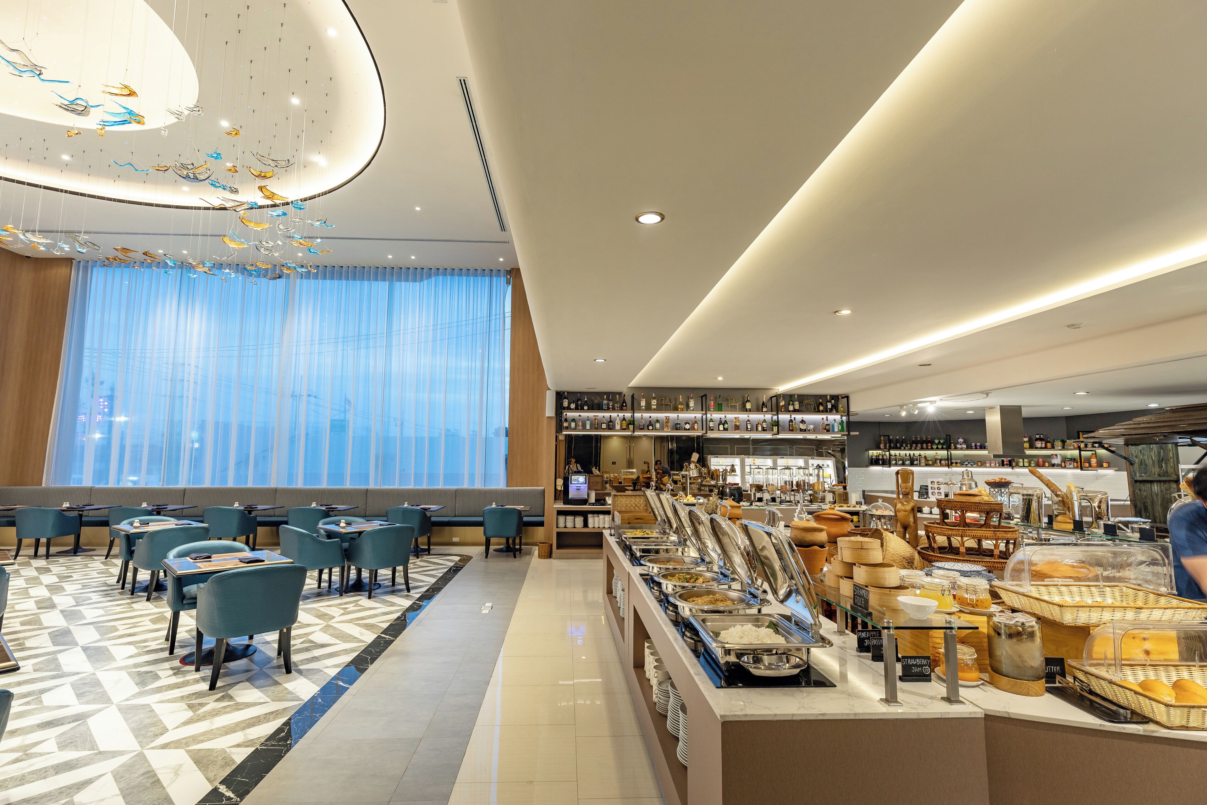 A hotel dining area with a buffet, seating, and a large window with curtains.