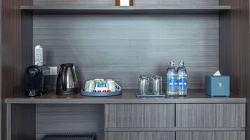Una kitchenette compacta con cafetera, hervidor y botellas de agua sobre una encimera de madera.