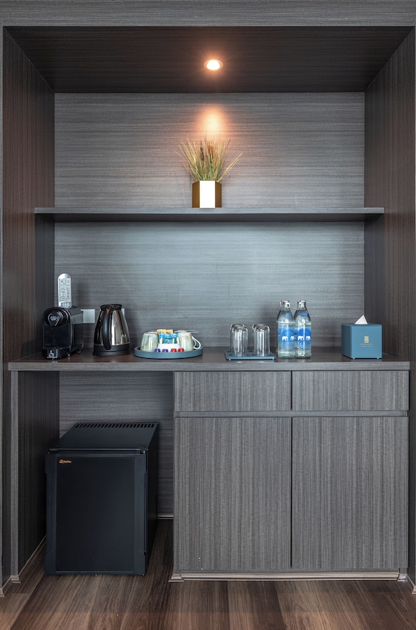 Una kitchenette compacta con cafetera, hervidor y botellas de agua sobre una encimera de madera.