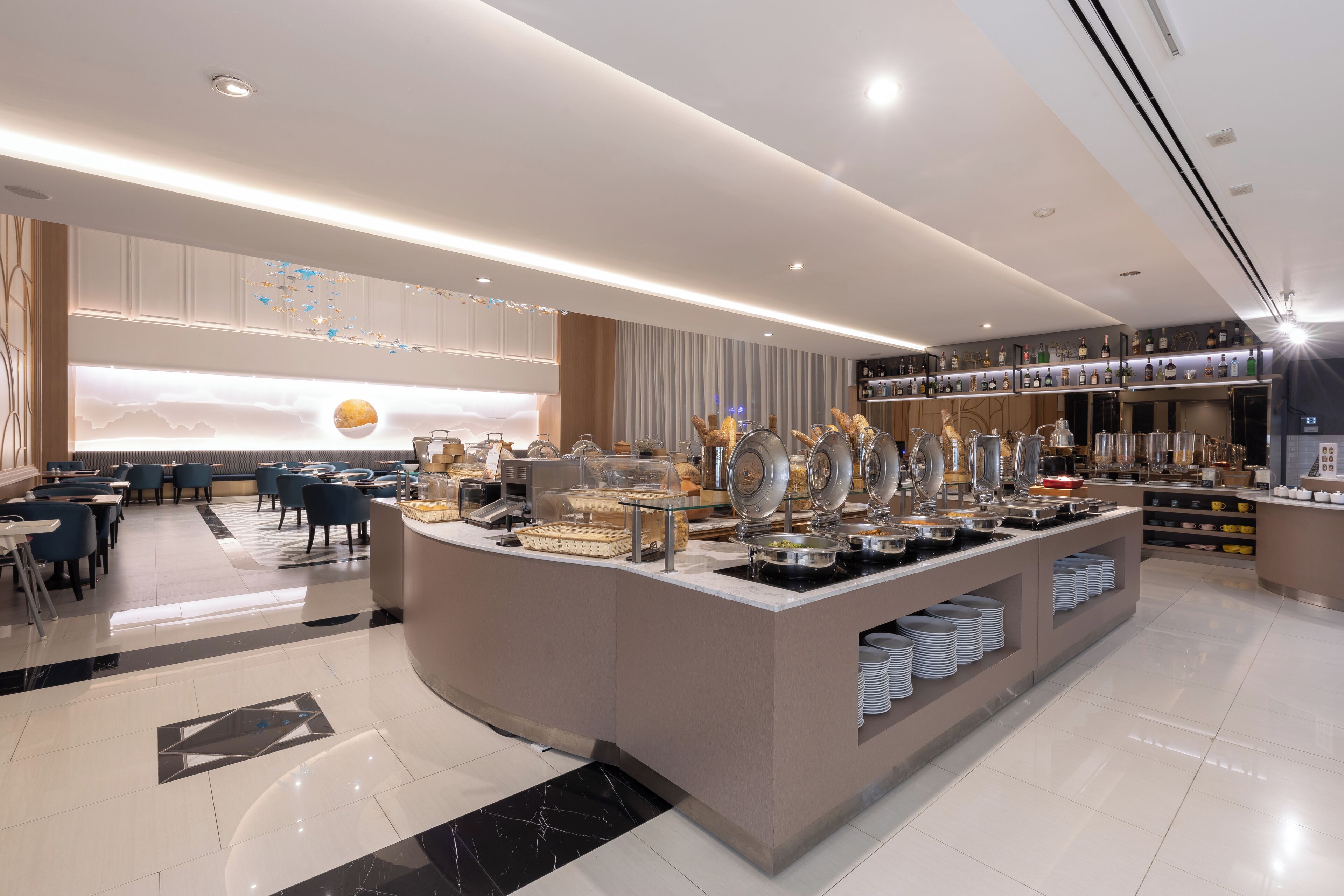 A modern hotel lobby with a buffet area, seating arrangements, and a bar.