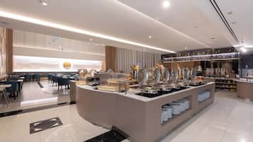 A modern hotel lobby with a buffet area, seating arrangements, and a bar.