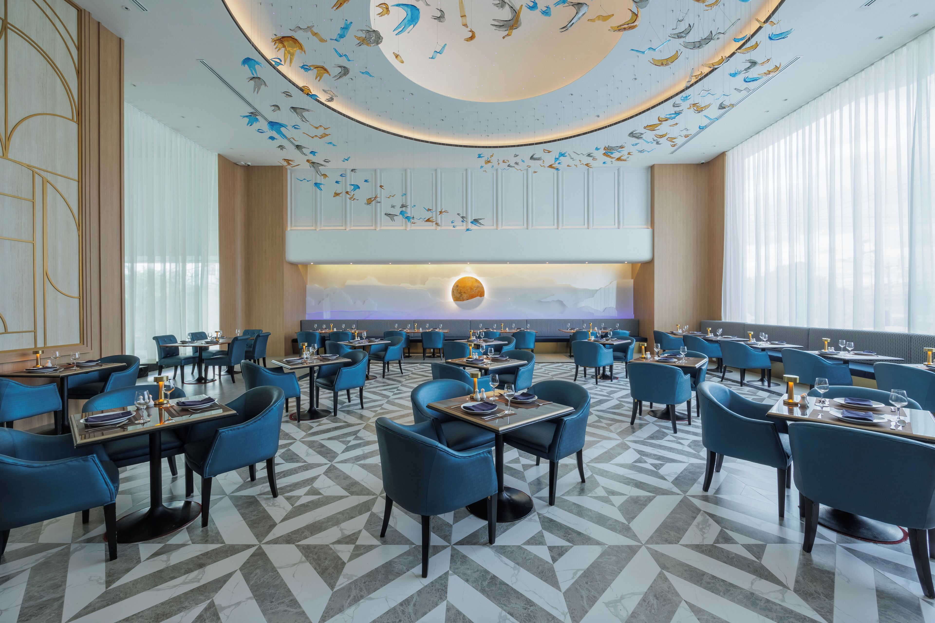 A modern restaurant with blue chairs and tables, a patterned floor, and a ceiling with bird illustrations.
