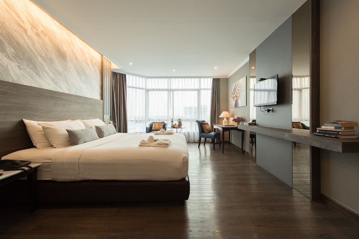 A modern hotel room with a large bed, a desk, a chair, and a TV.