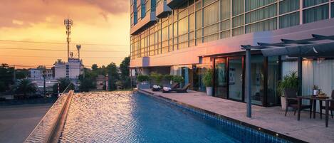 A swimming pool adjacent to a modern building with large windows and a covered outdoor seating area.