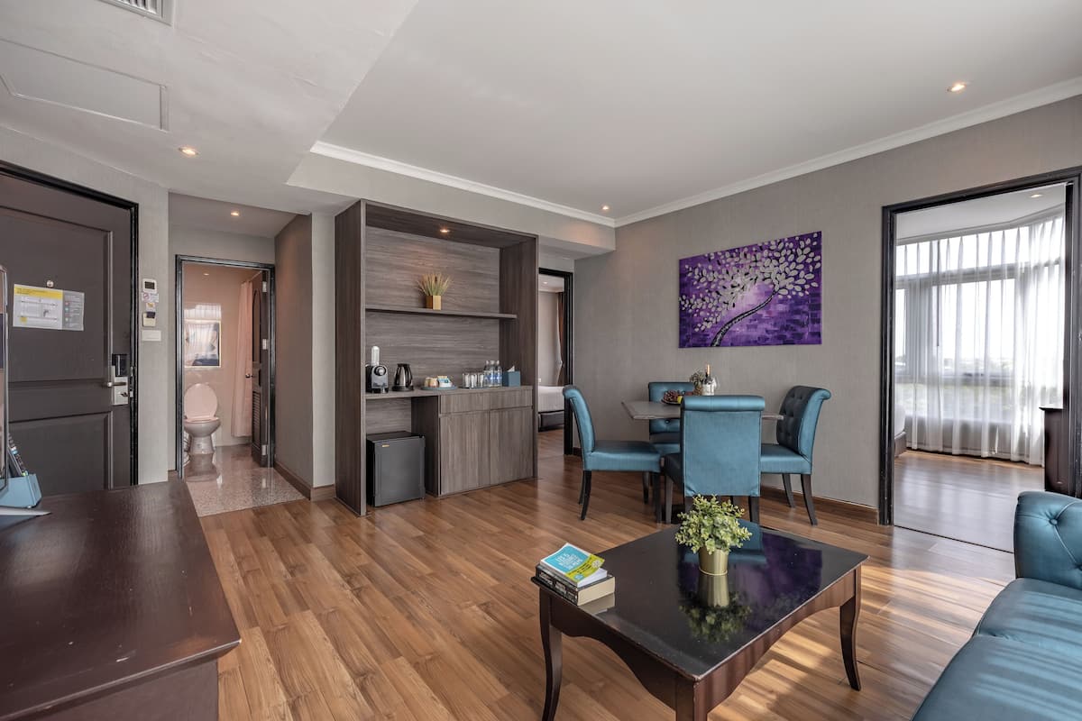 A modern living room with a wooden floor, a dining area with blue chairs, a kitchen with a built-in island, and a purple artwork on the wall.