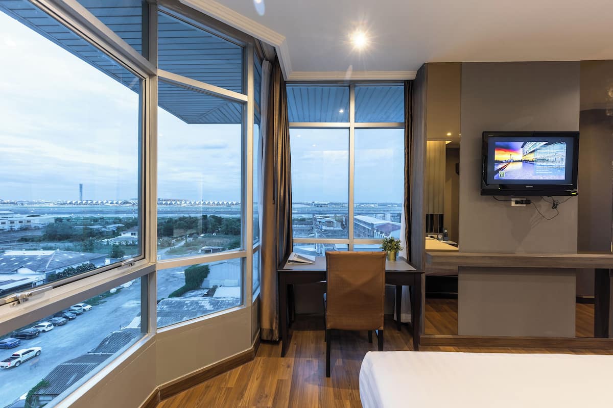 A hotel room with a large window, a desk, a chair, a bed, and a TV mounted on the wall.