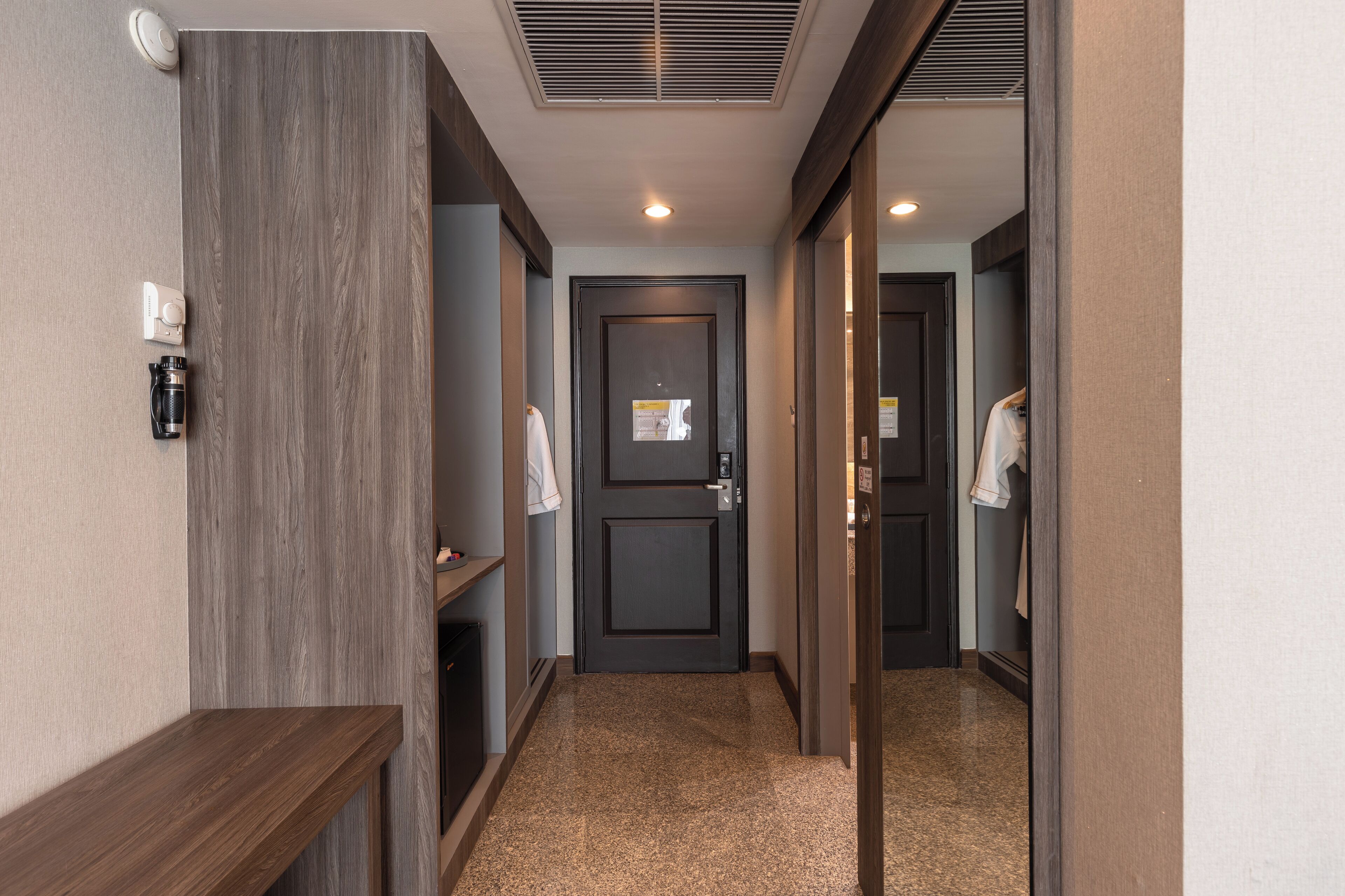 A hallway with a dark door, a coat rack, and a small shelf with a coffee maker.