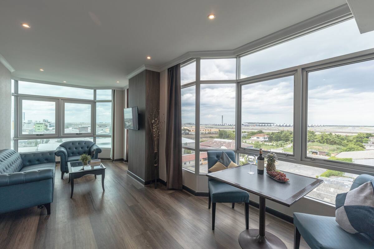 A spacious living room with large windows, a flat-screen TV, and a dining area with a table and chairs.