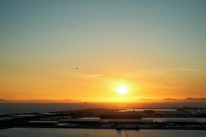 A sunset over a coastal area with a large ship docked at a port. - Kanku Izumiotsu Washington Hotel (Izumiotsu)