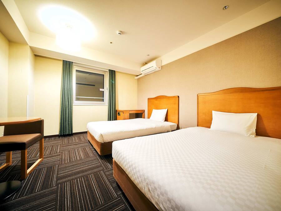 A hotel room with two beds, a desk, and a chair.
