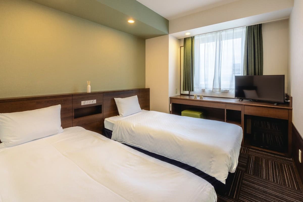 Une chambre d’hôtel avec deux lits, un bureau avec une télévision et une fenêtre avec des rideaux.
