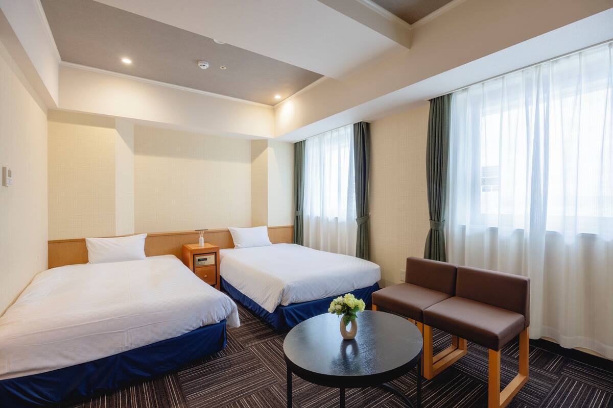 Une chambre d’hôtel avec deux lits, un canapé, une petite table et un vase de fleurs.