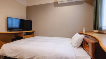 A hotel room with a bed, a TV, a desk, and an air conditioning unit.