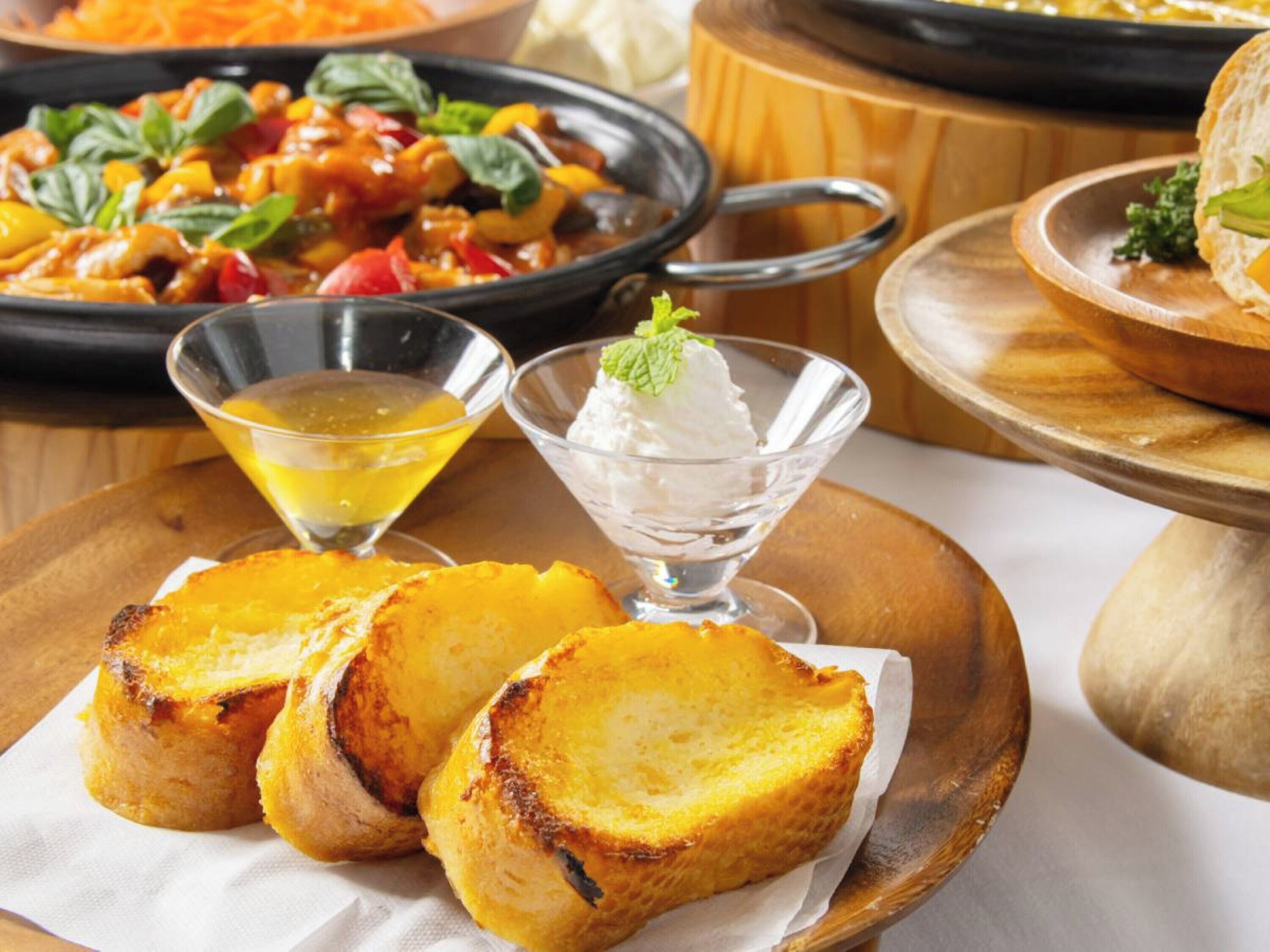 Uma mesa com pratos de comida, incluindo pão grelhado, uma sobremesa e um prato com legumes.