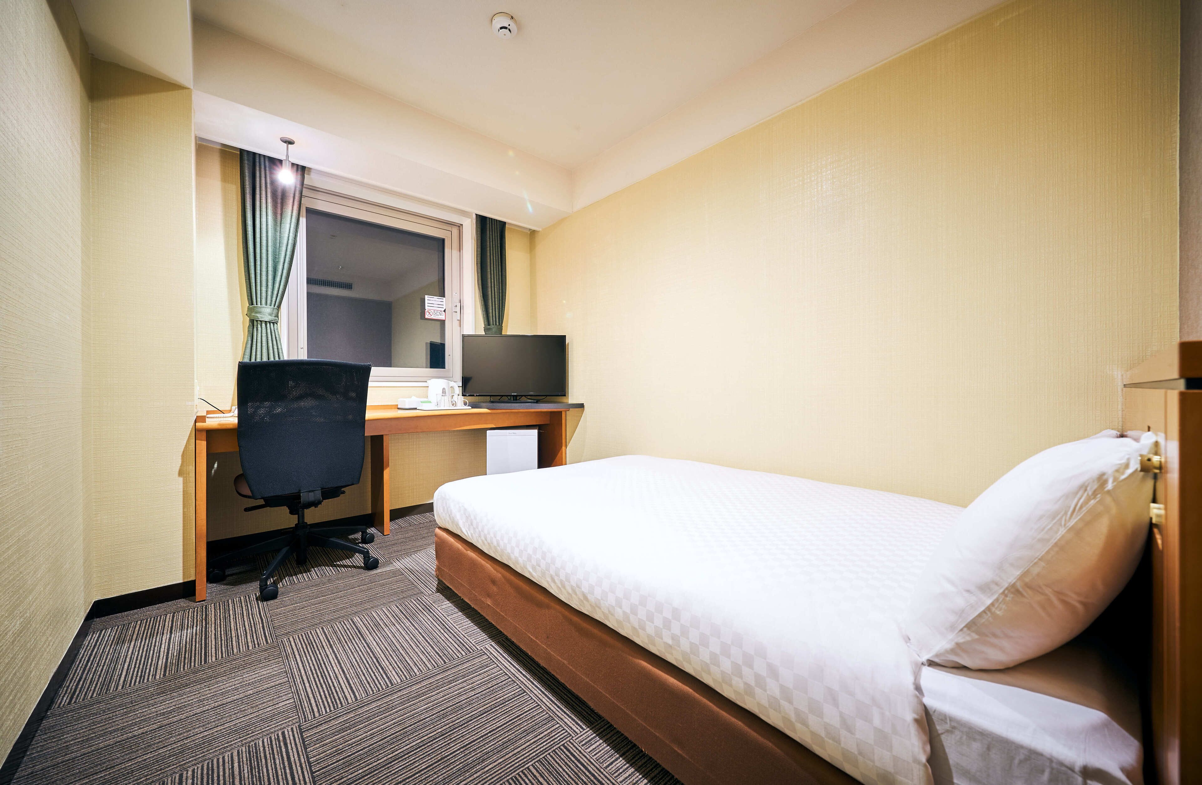 A hotel room with a single bed, a desk with a computer, and a chair.
