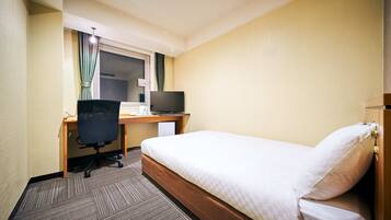 A hotel room with a single bed, a desk with a computer, and a chair.