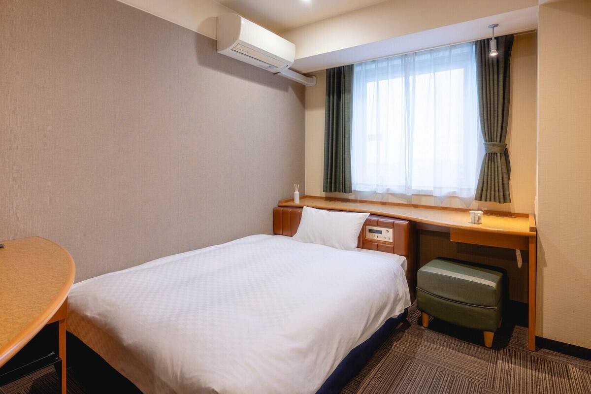Une chambre d’hôtel équipée d’un lit, d’un bureau, d’une chaise, d’une télévision, d’une fenêtre avec des rideaux et d’un appareil de climatisation.