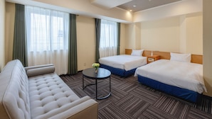 A hotel room with a sofa, two beds, a small table with a vase, and a nightstand.