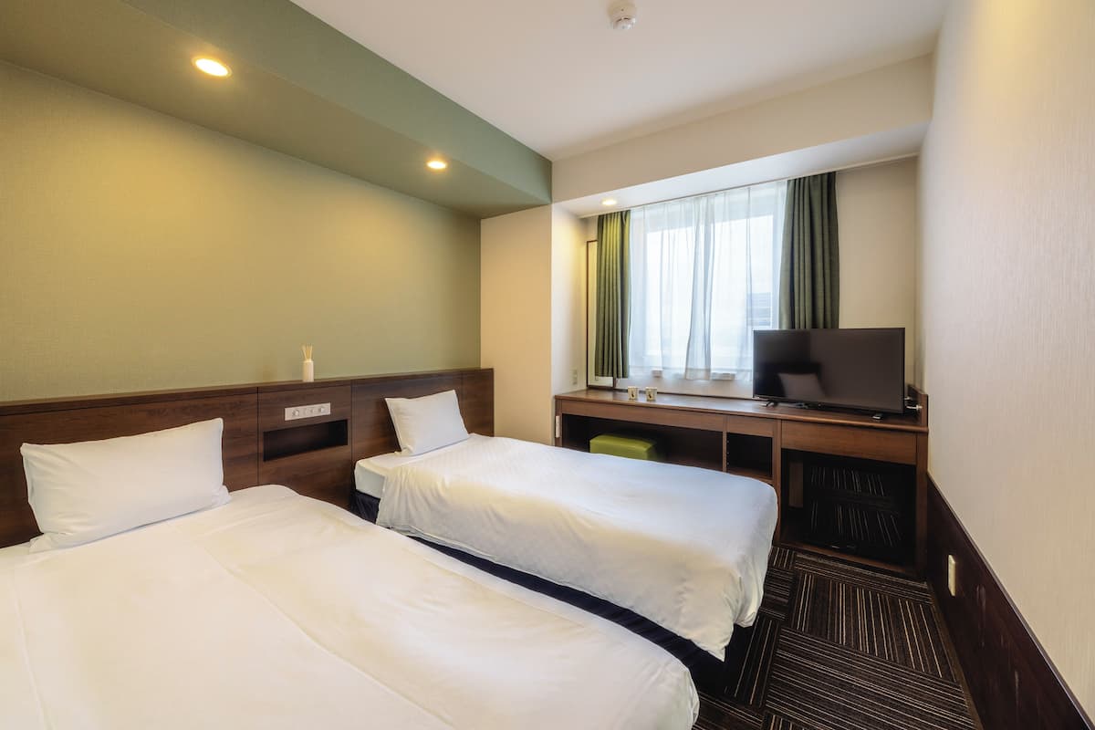 Une chambre d’hôtel avec deux lits, un bureau avec une télévision et une fenêtre avec des rideaux.