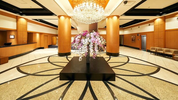 A spacious lobby with a central floral arrangement, a chandelier, and a reception desk.