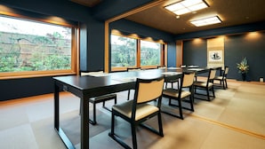 A conference room with a long table and chairs, large windows with a view of a garden, and a ceiling with recessed lighting.