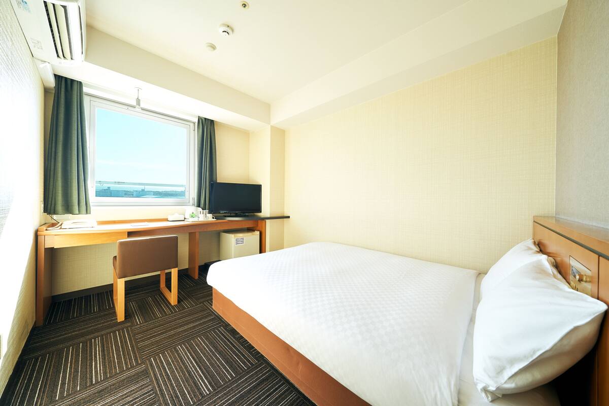 Une chambre d’hôtel équipée d’un lit, d’un bureau, d’une chaise, d’une télévision et d’une fenêtre avec des rideaux.