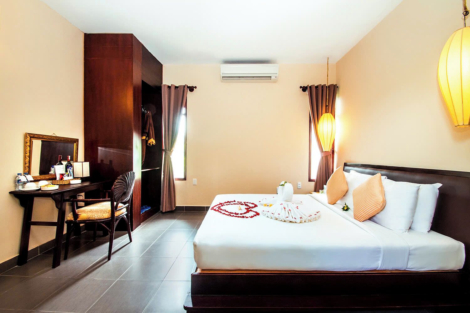 A hotel room with a bed, a desk, a chair, a mirror, and a wall-mounted air conditioner.