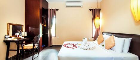 A hotel room with a bed, a desk, a chair, a mirror, and a wall-mounted air conditioner.